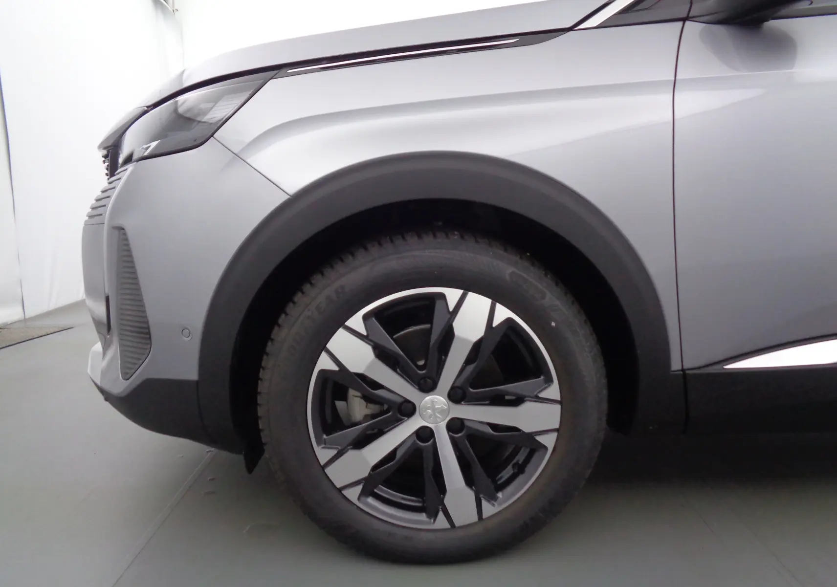 Gros plan sur la roue avant gauche d'un Peugeot 3008 gris Artense métal avec jante alliage bicolore.
