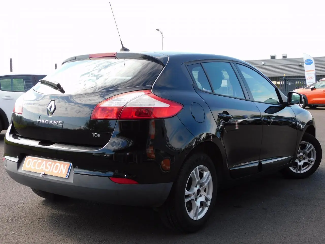 Renault Mégane noire vue en 3/4 arrière droit sur parking, avec feux arrière et jantes visibles.