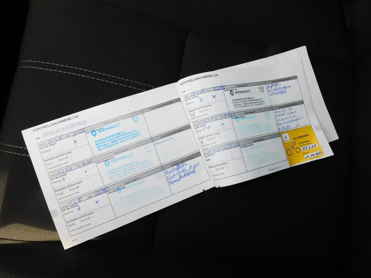 Carnet d'entretien Renault posé sur un siège noir avec surpiqûres blanches, vue rapprochée intérieure.