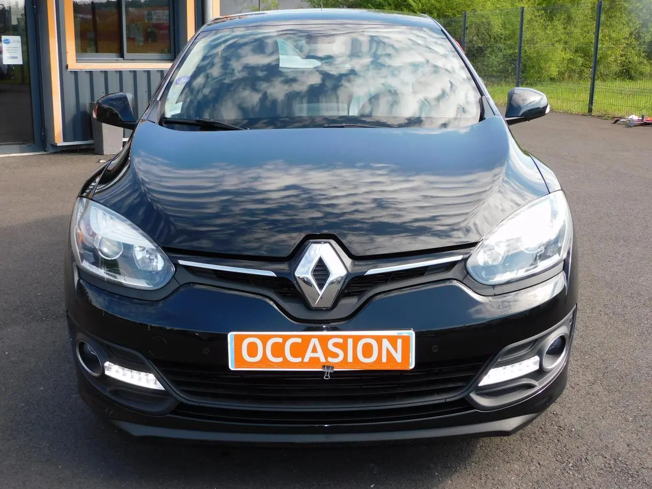 Vue avant d'une Renault Mégane noire 2015 avec phares allumés et plaque orange "OCCASION" visible.