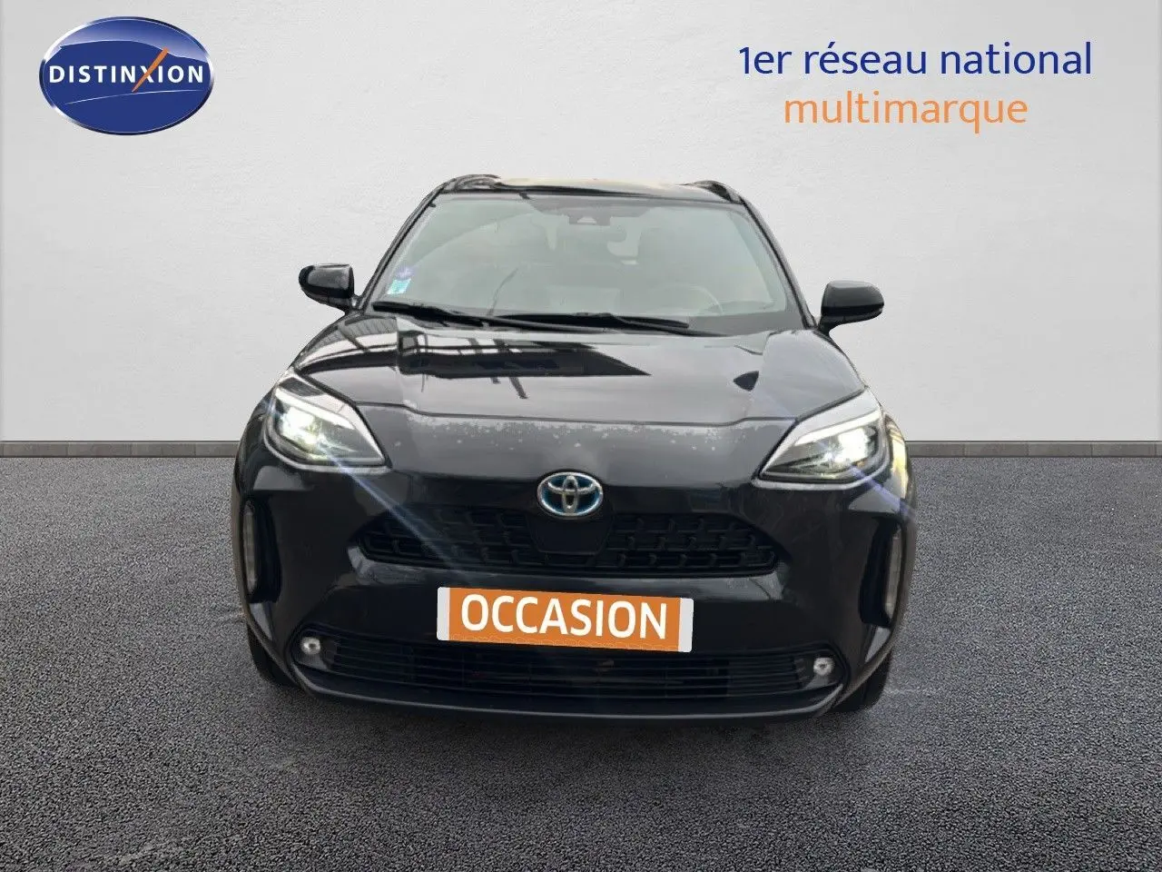 Vue frontale d'une Toyota Yaris Cross 116h Design noire de 2023 avec phares allumés sur fond neutre.