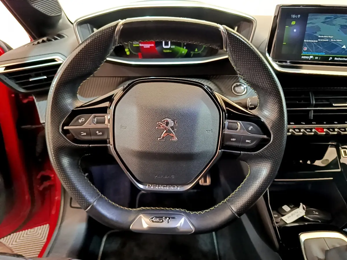 Vue rapprochée du volant cuir GT Line de la Peugeot 208 rouge 2020 avec tableau de bord numérique et écran tactile.