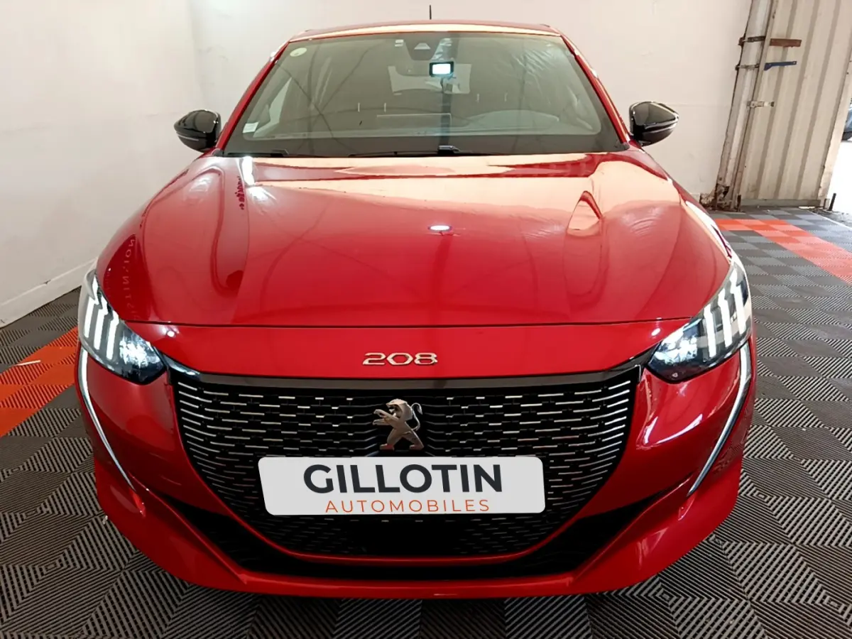 Vue frontale d'une Peugeot 208 BlueHDi 100 S&S GT Line rouge avec phares LED allumés et calandre noire distinctive.