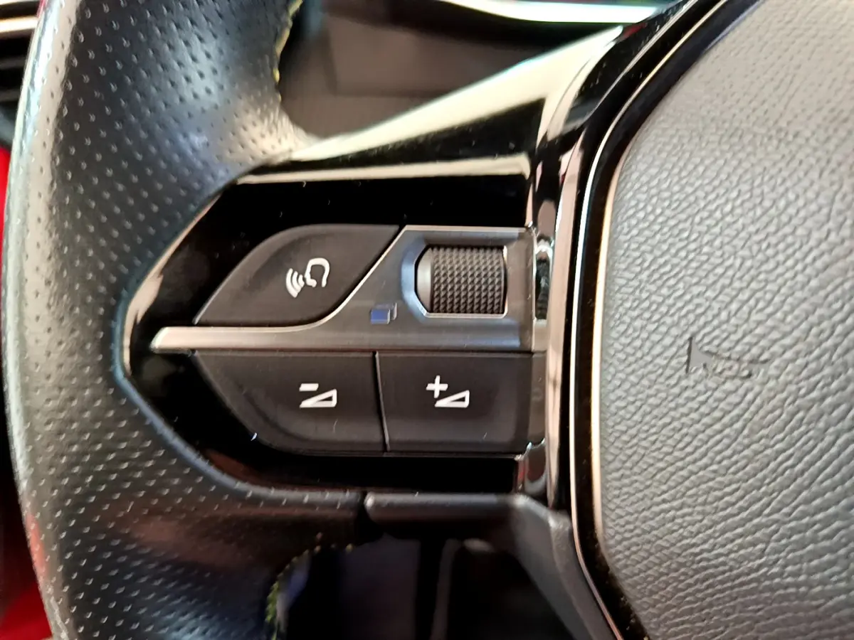 Gros plan sur les commandes vocales et volume du volant en cuir perforé de la Peugeot 208 GT Line rouge.