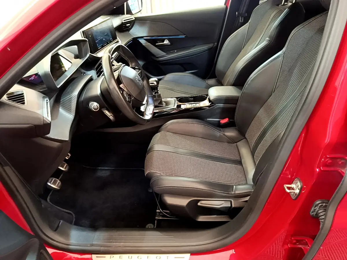 Intérieur côté conducteur de la Peugeot 208 rouge, montrant sièges sport et tableau de bord moderne avec écran tactile.