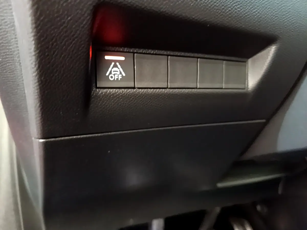 Gros plan sur le bouton d'arrêt de l'assistance au maintien de voie dans l'habitacle noir de la Peugeot 208 GT Line rouge.