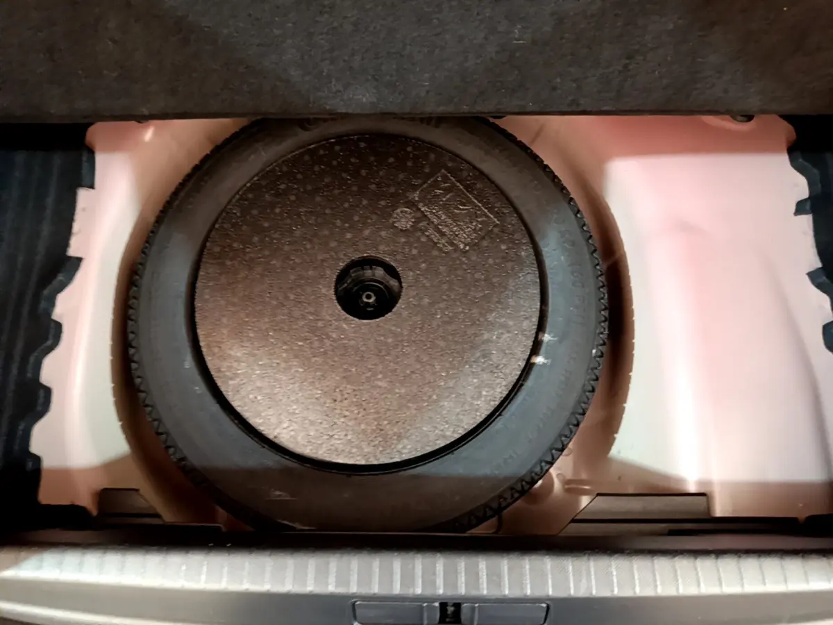 Roue galette de secours noire dans le coffre blanc d'une Peugeot 208 GT Line rouge, vue en plongée.