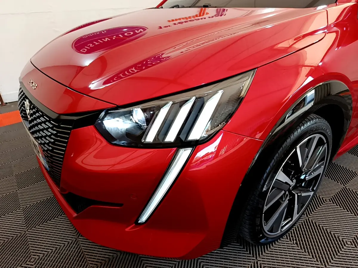 Vue 3/4 avant droit du Peugeot 208 rouge avec ses phares LED distinctifs en forme de griffes et jante alliage moderne.