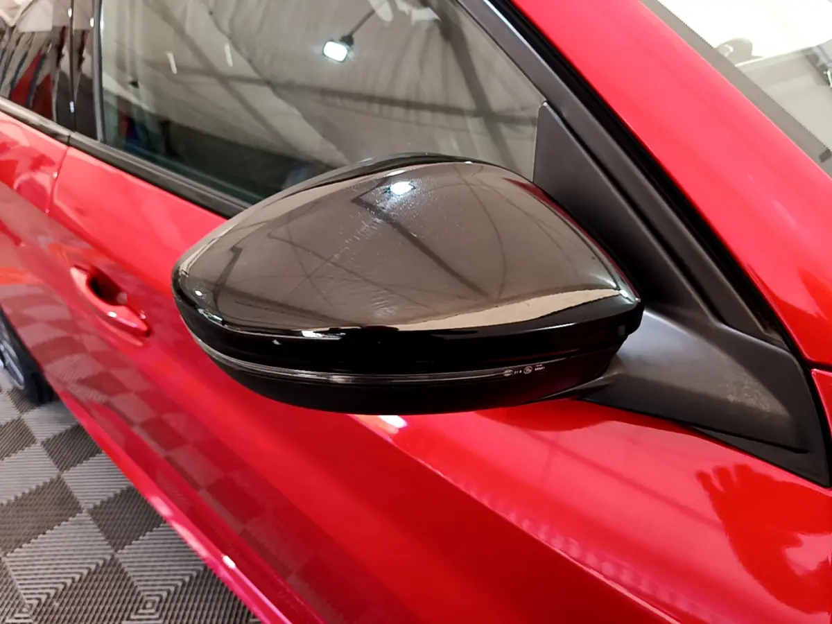 Rétroviseur noir brillant côté gauche d'une Peugeot 208 rouge vue de près sur porte avant.