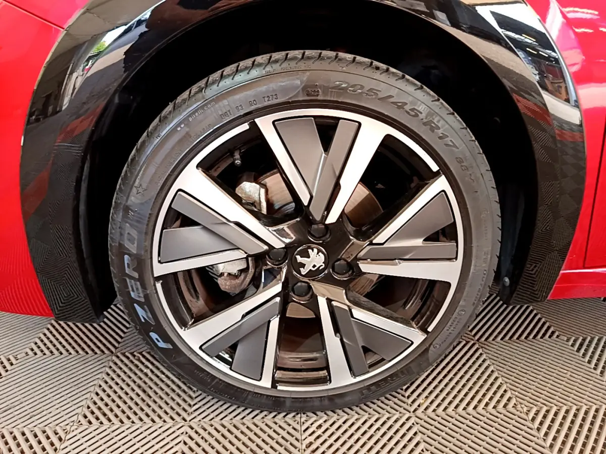 Gros plan sur la roue avant droite de la Peugeot 208 rouge avec jante alliage à design moderne et logo lion central.