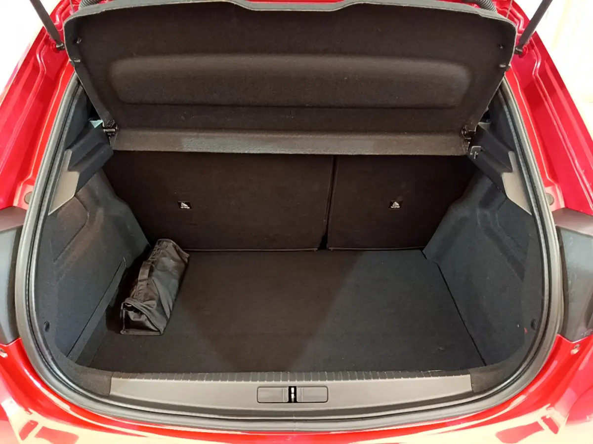 Coffre ouvert vu de l'arrière d'une Peugeot 208 rouge, montrant un espace de rangement propre et vide.