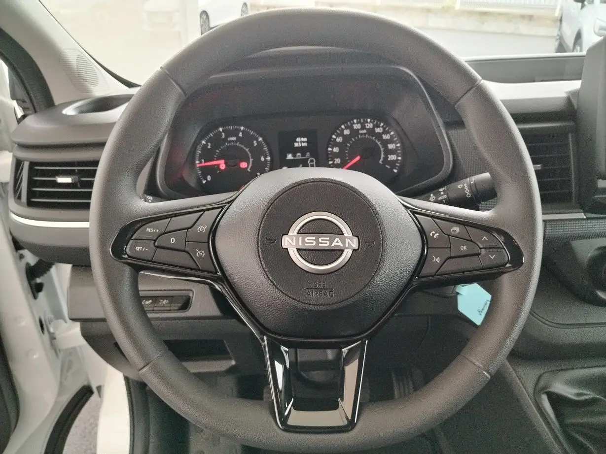 Vue centrée sur le volant noir du Nissan Primastar 2025, avec tableau de bord et commandes visibles en arrière-plan.