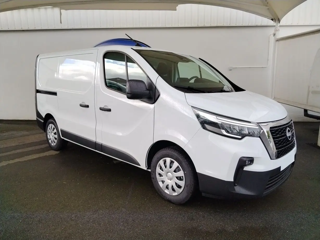 Vue 3/4 avant droit d'un utilitaire Nissan Primastar blanc avec calandre noire et jantes tôles sous abri.