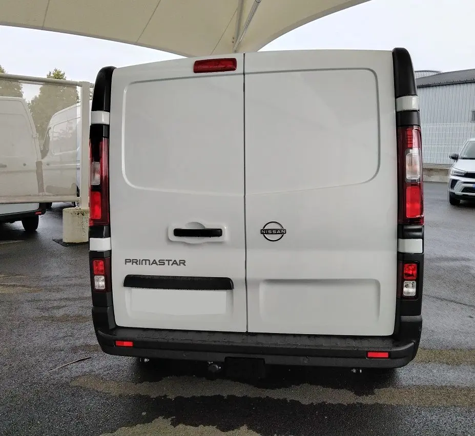 Vue arrière d'un utilitaire blanc Nissan Primastar 2025 avec porte battante et attelage visible.