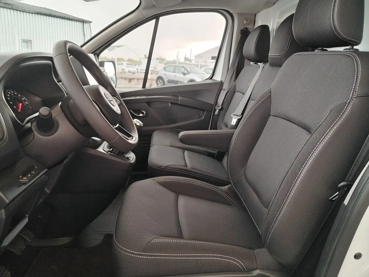 Vue intérieure côté conducteur du Nissan Primastar 2025 blanc, sièges noirs avec coutures blanches et volant multifonction.