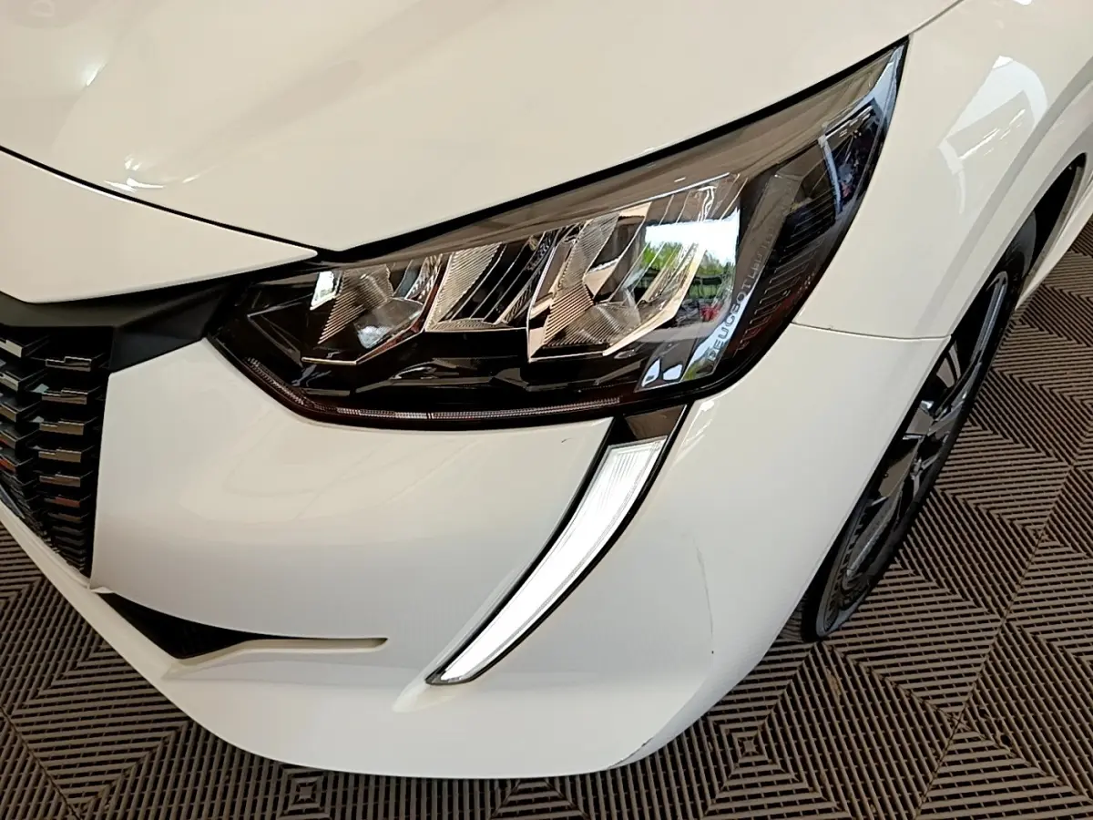 Gros plan sur le phare avant droit blanc du Peugeot 208 avec sa signature lumineuse LED distinctive.