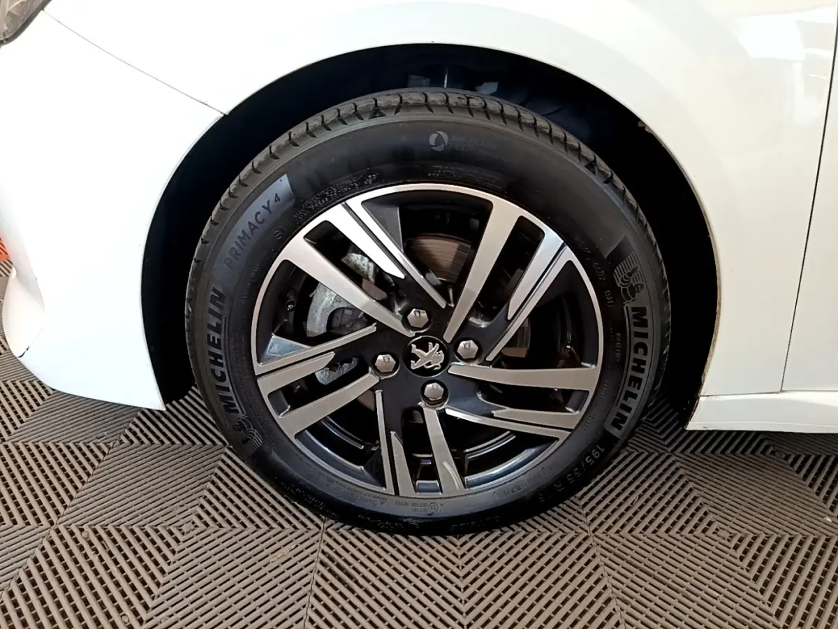 Gros plan sur la roue avant droite d'une Peugeot 208 blanche, jante alliage noire et argent avec pneu Michelin.