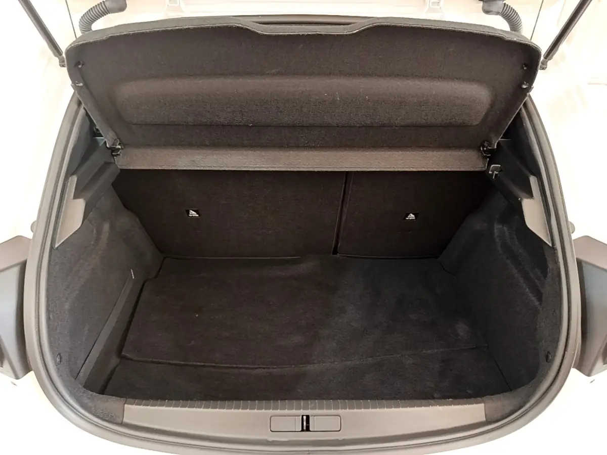 Coffre ouvert vu de l'arrière d'une Peugeot 208 blanche, montrant un espace de chargement propre et vide.