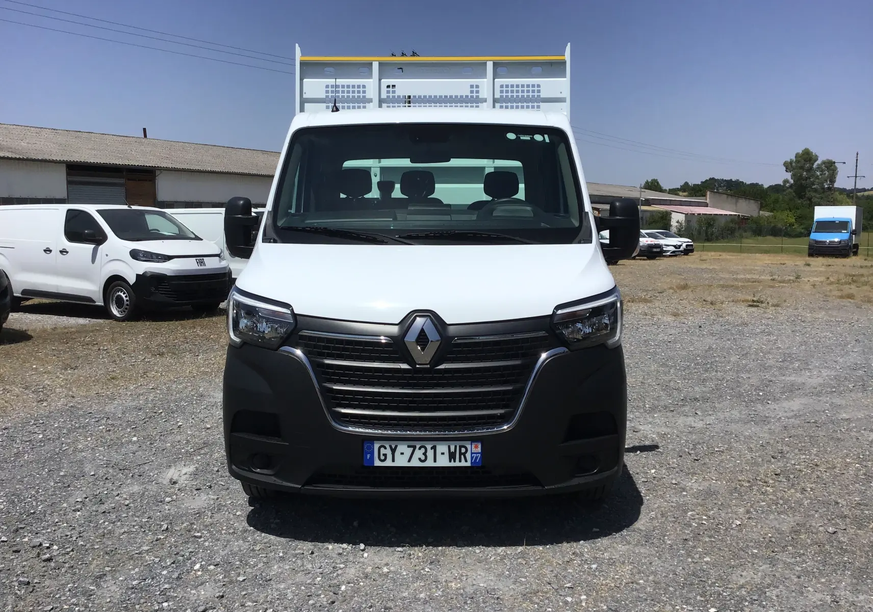 Vue frontale d’un Renault Master Châssis Cabine blanc 2024 avec benne et calandre noire, sur un terrain extérieur.