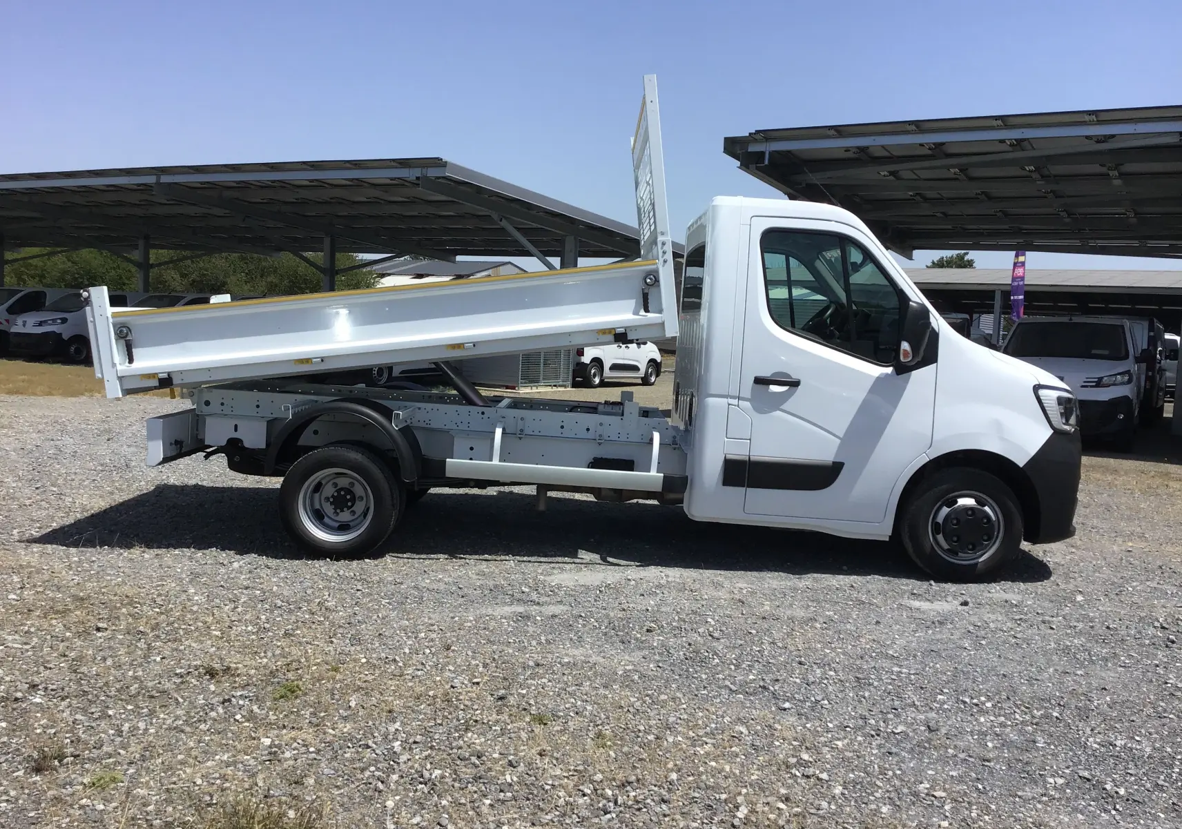 Renault Master benne blanche vue de profil côté gauche, benne relevée et roues jumelées arrière visibles.