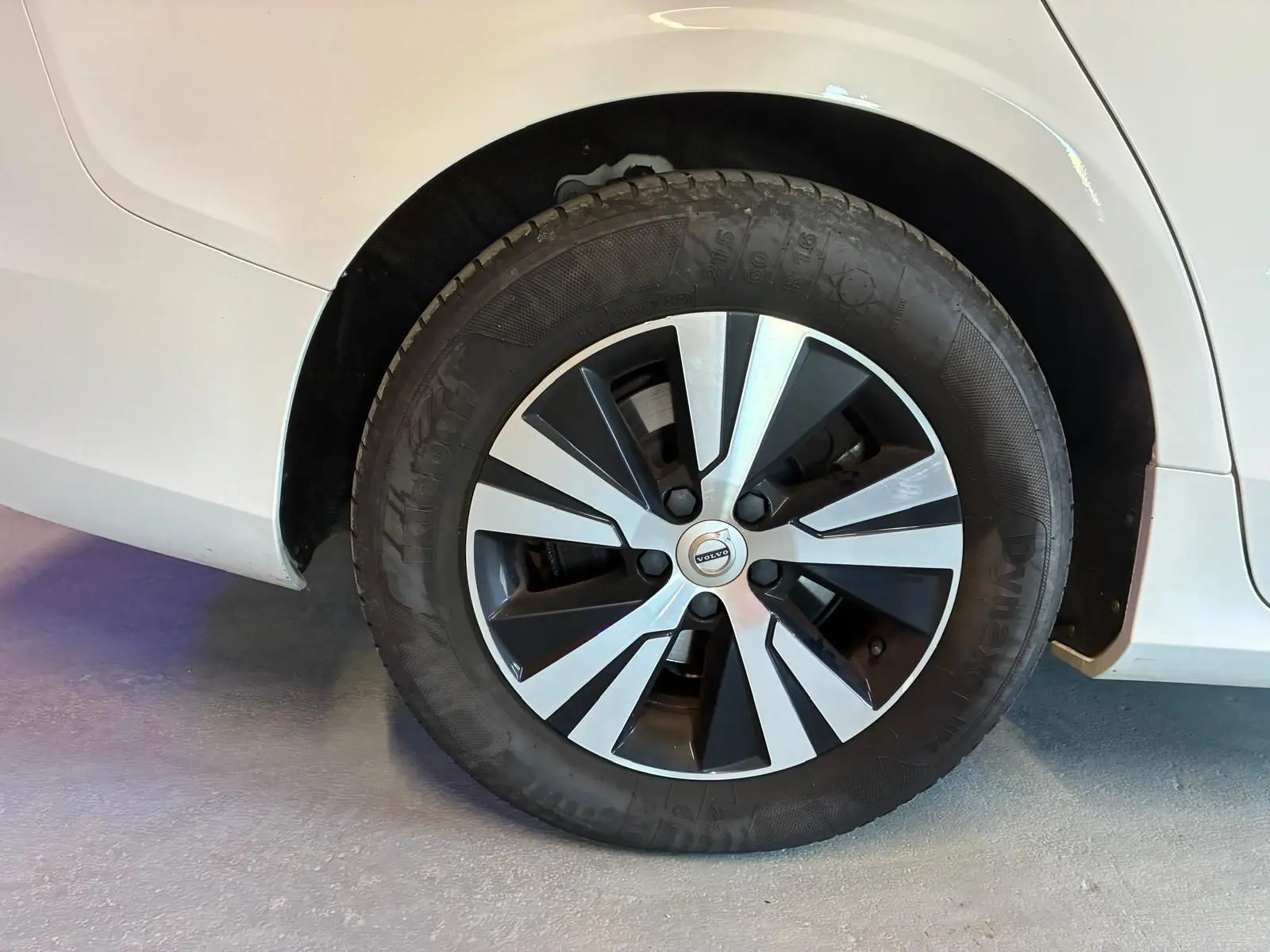 Gros plan sur la roue avant droite d'une Volvo V60 blanche, jante alliage bicolore au design moderne.