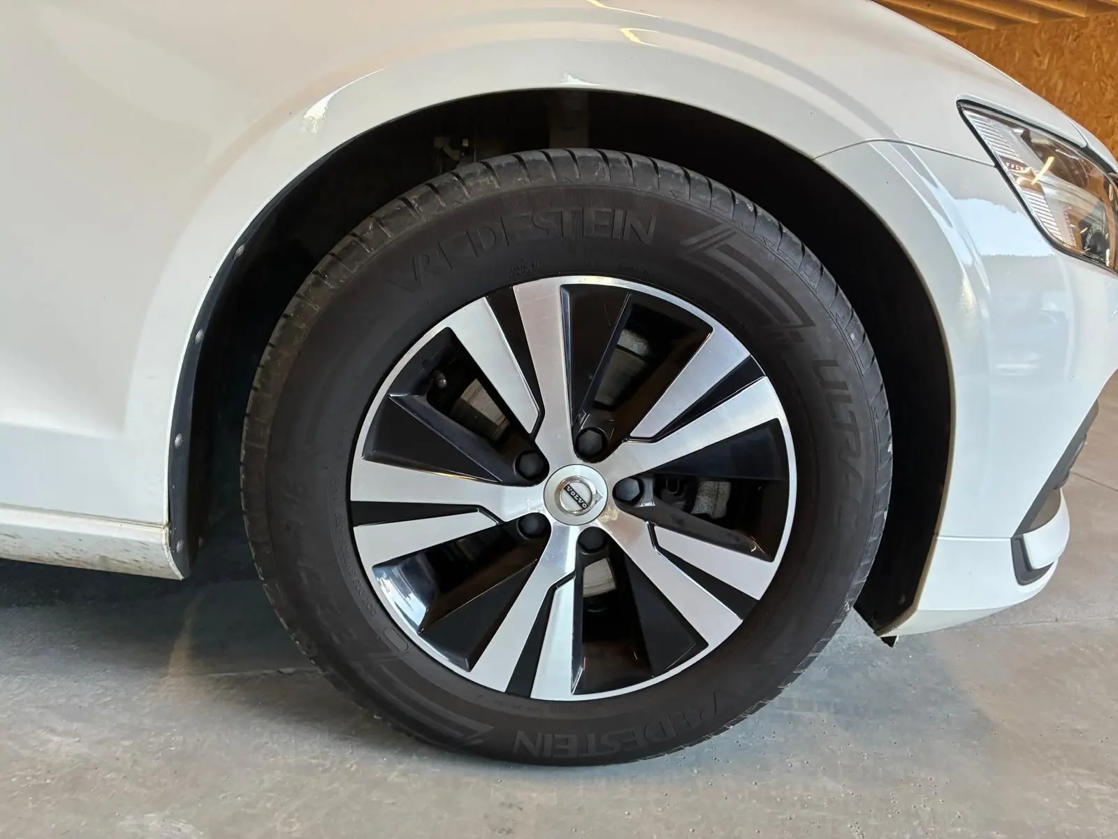 Gros plan sur la roue avant droite d’une Volvo V60 blanche de 2020, jante alliage bicolore et pneu Vredestein.