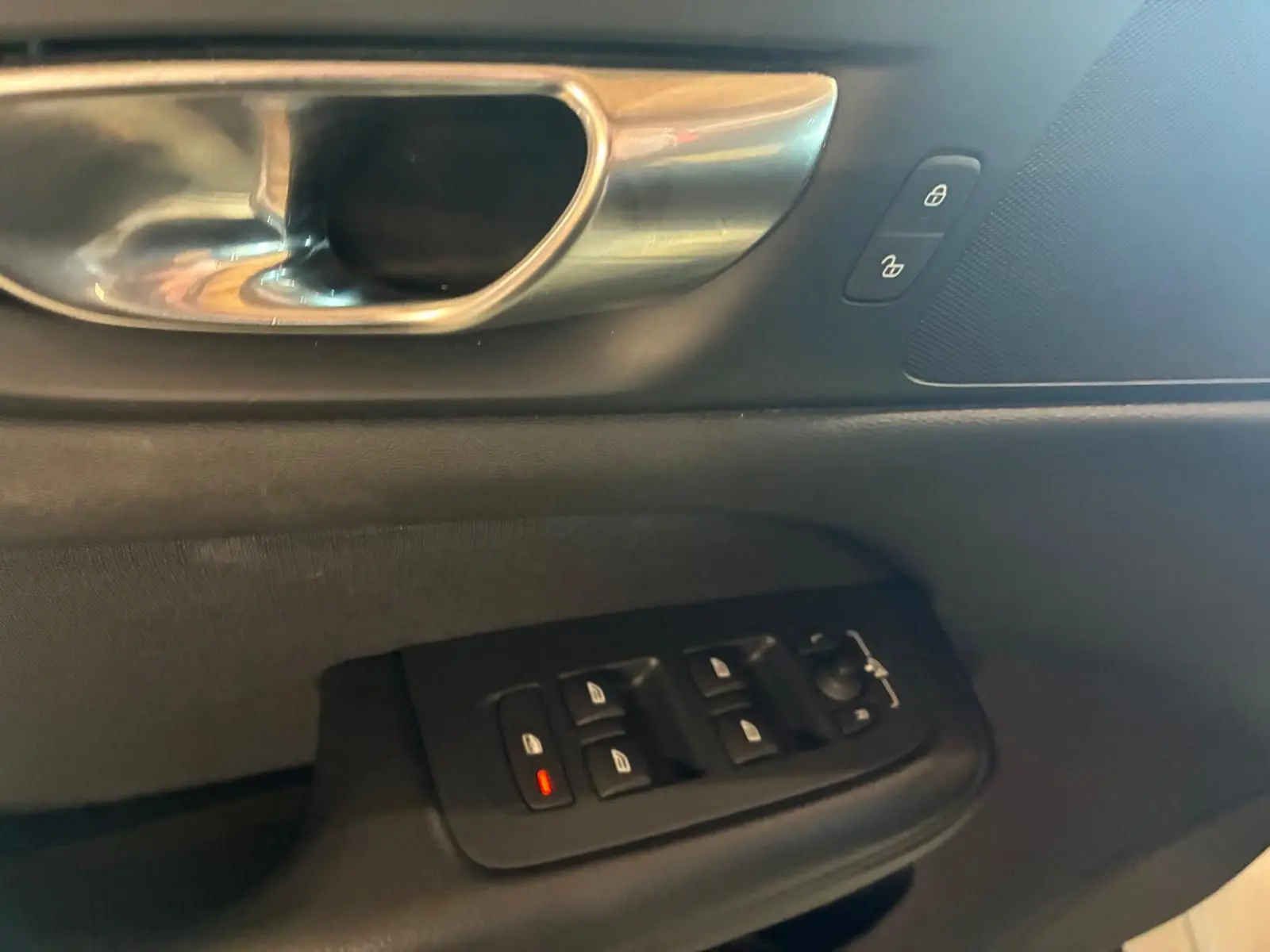 Gros plan sur la poignée intérieure et les commandes des vitres côté conducteur d’un Volvo V60 D3 blanc, intérieur noir.