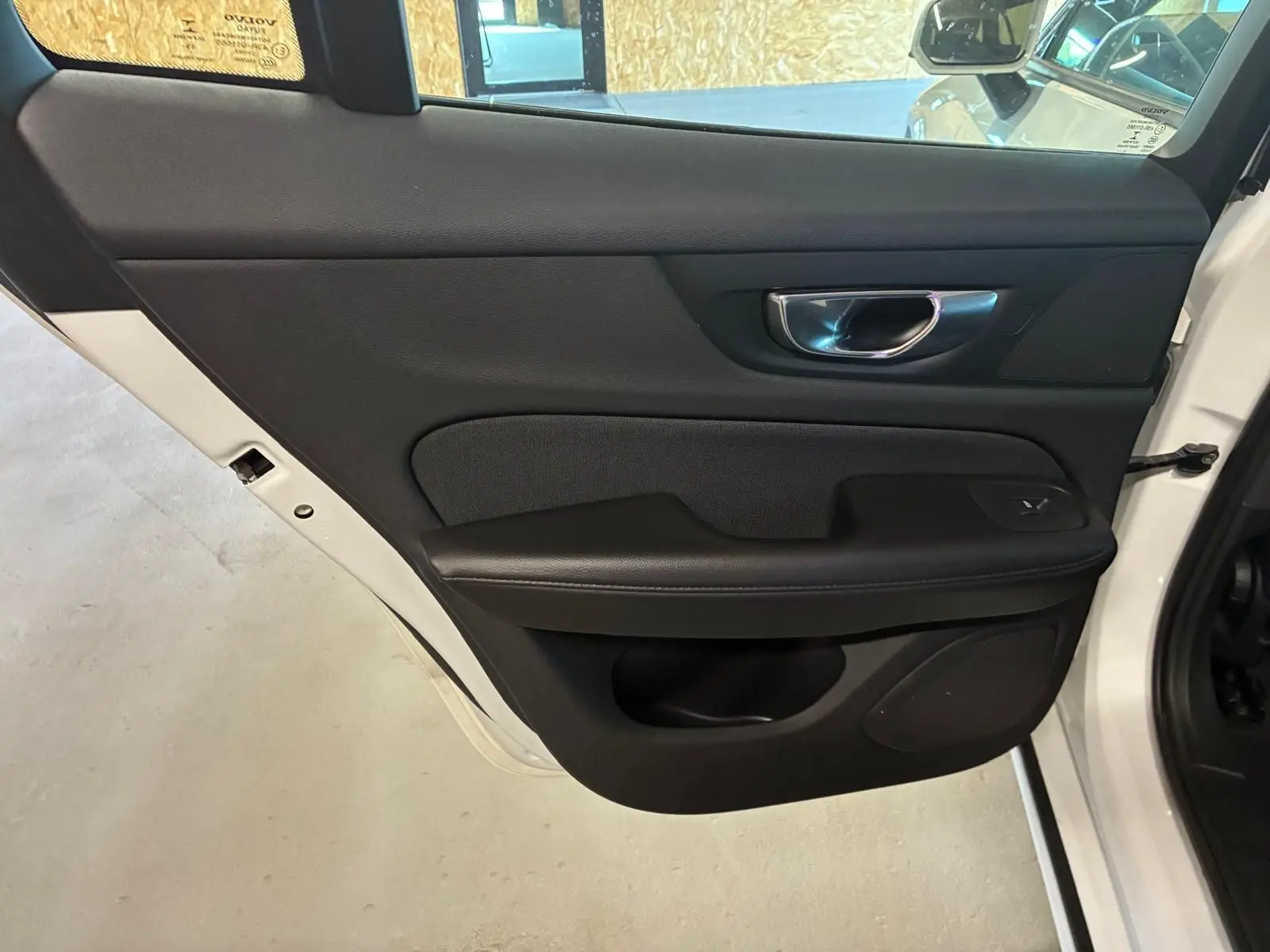 Vue rapprochée de la porte arrière gauche noire intérieure du Volvo V60 blanc, avec poignée chromée et bouton de vitre.