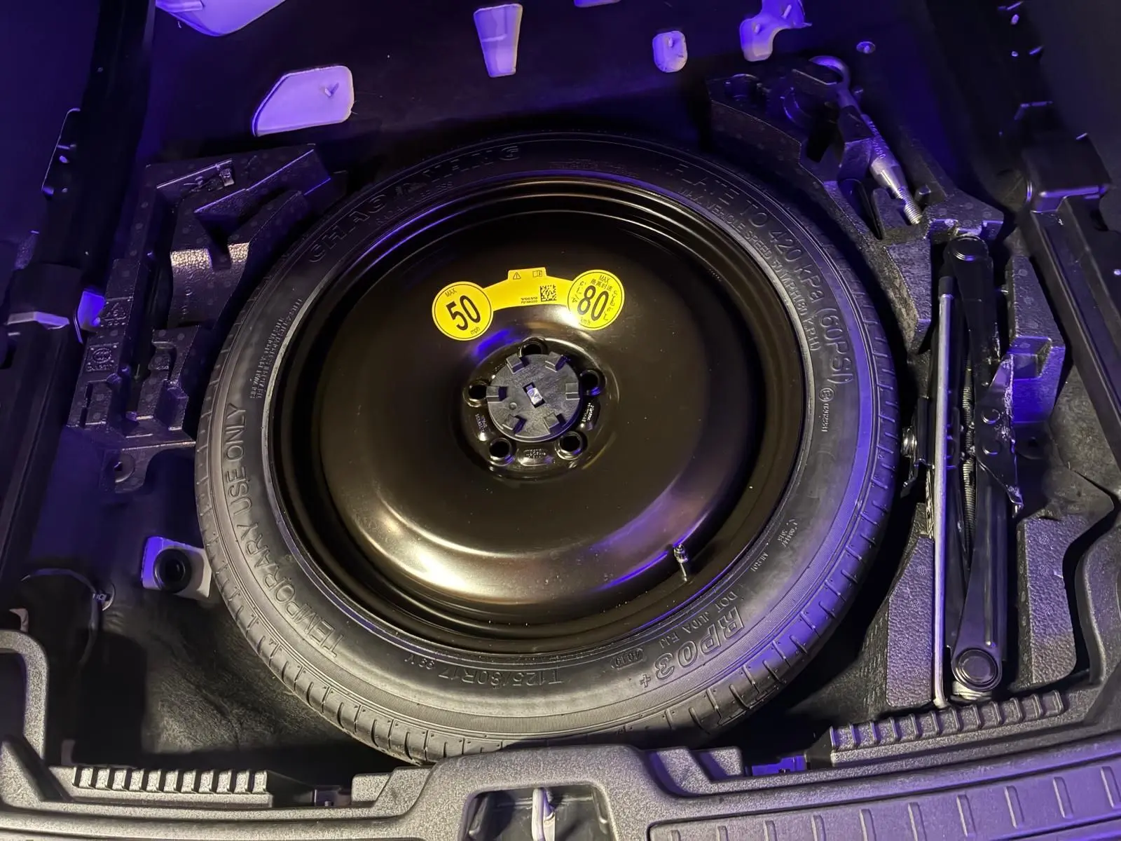 Vue plongeante sur la roue de secours noire et les outils de coffre du Volvo V60 blanc, version D3 2020.
