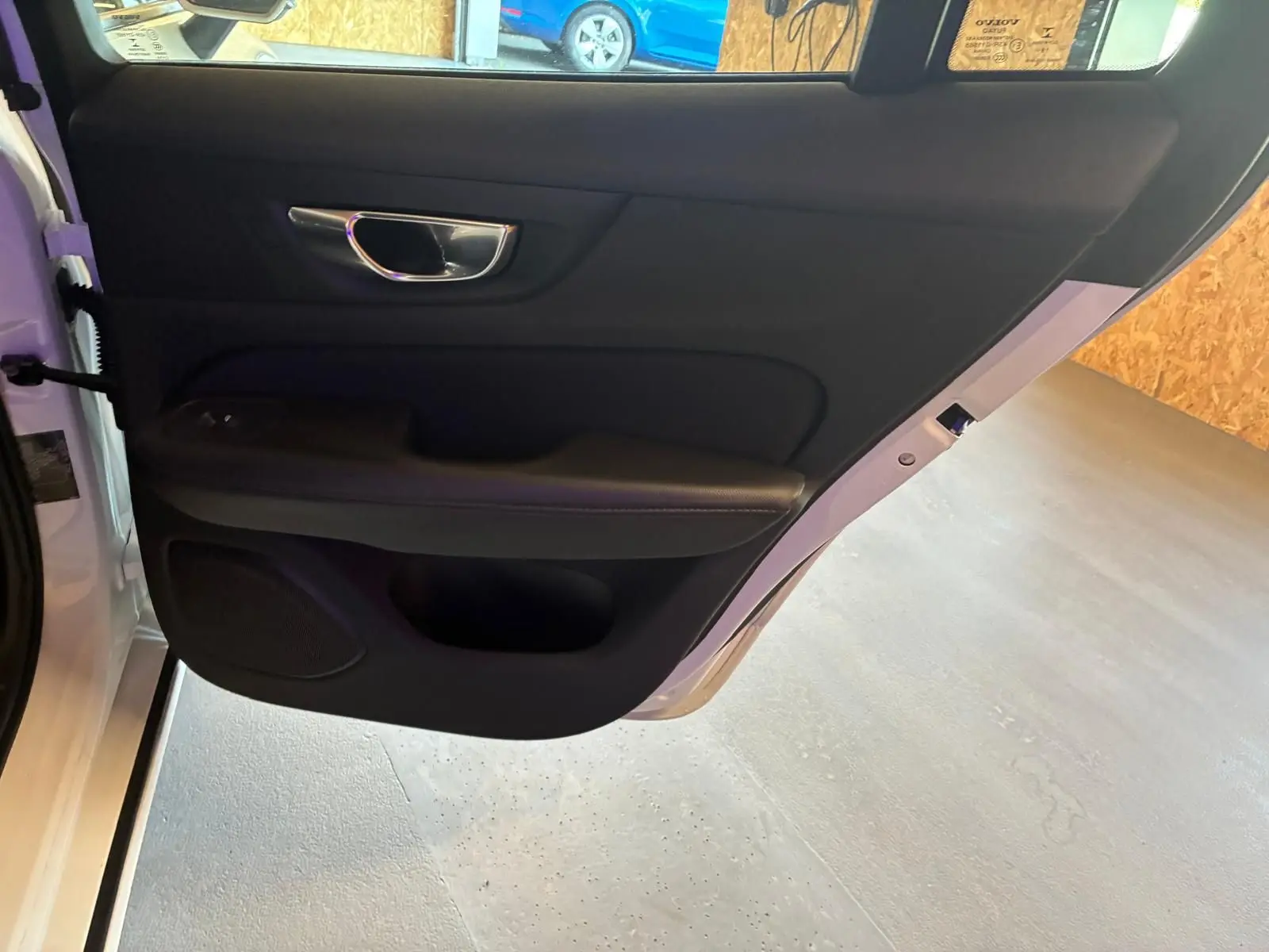 Vue intérieure de la porte arrière gauche noire d'une Volvo V60 D3 blanche, avec poignée chromée et haut-parleur intégré.