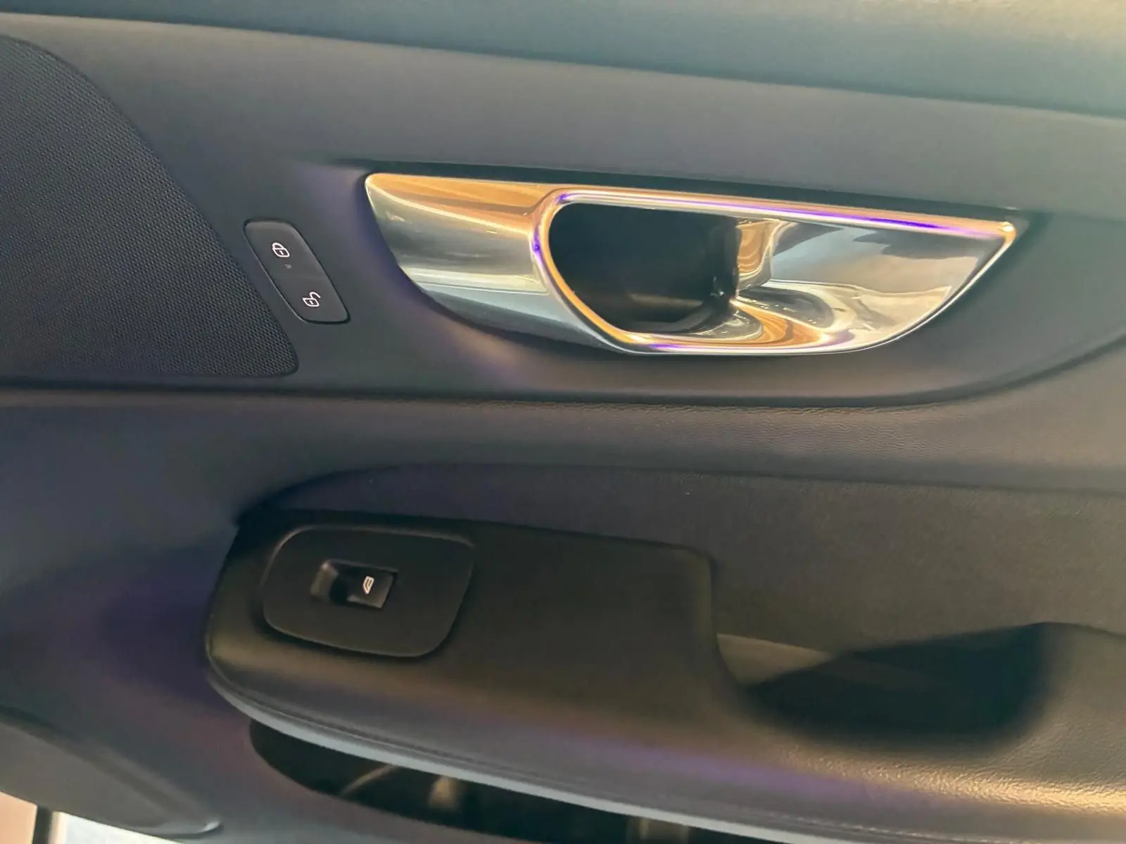 Poignée intérieure chromée et commandes de verrouillage sur la porte côté gauche d’un Volvo V60 blanc, vue rapprochée.
