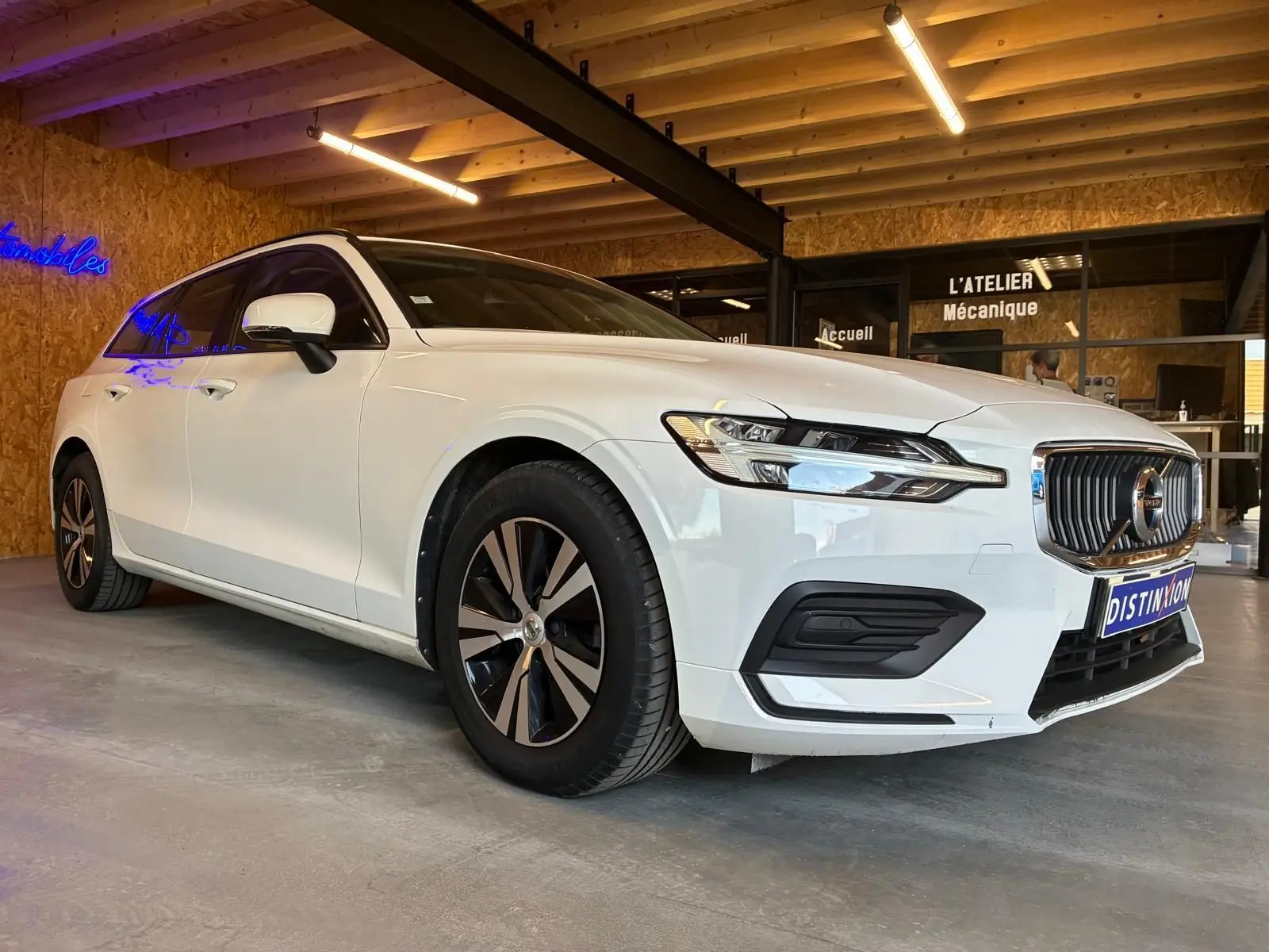 Volvo V60 D3 blanche vue en 3/4 avant droit, avec calandre chromée et jantes bi-ton dans un garage.
