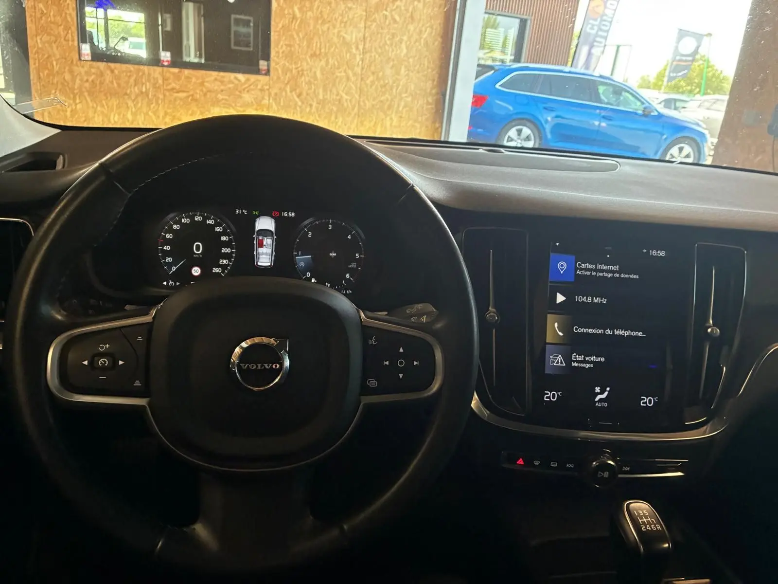 Vue intérieure centrée sur le volant et le tableau de bord noir d'une Volvo V60 blanche, avec écran tactile allumé.