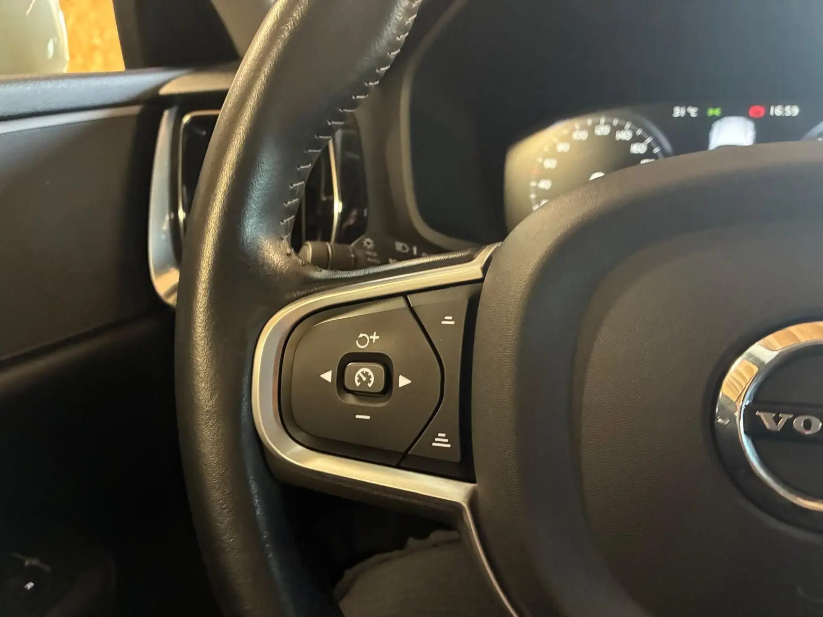 Gros plan sur le volant côté gauche d’un Volvo V60 blanc, montrant les commandes de régulateur de vitesse et le tableau de bord flou.