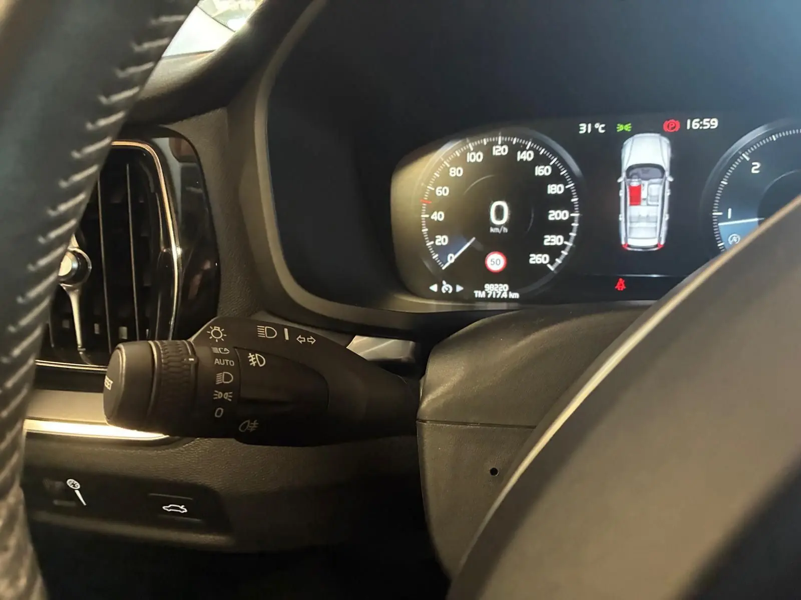 Vue rapprochée du combiné d'instruments et du commodo d'éclairage noir dans le tableau de bord d'une Volvo V60 blanche.