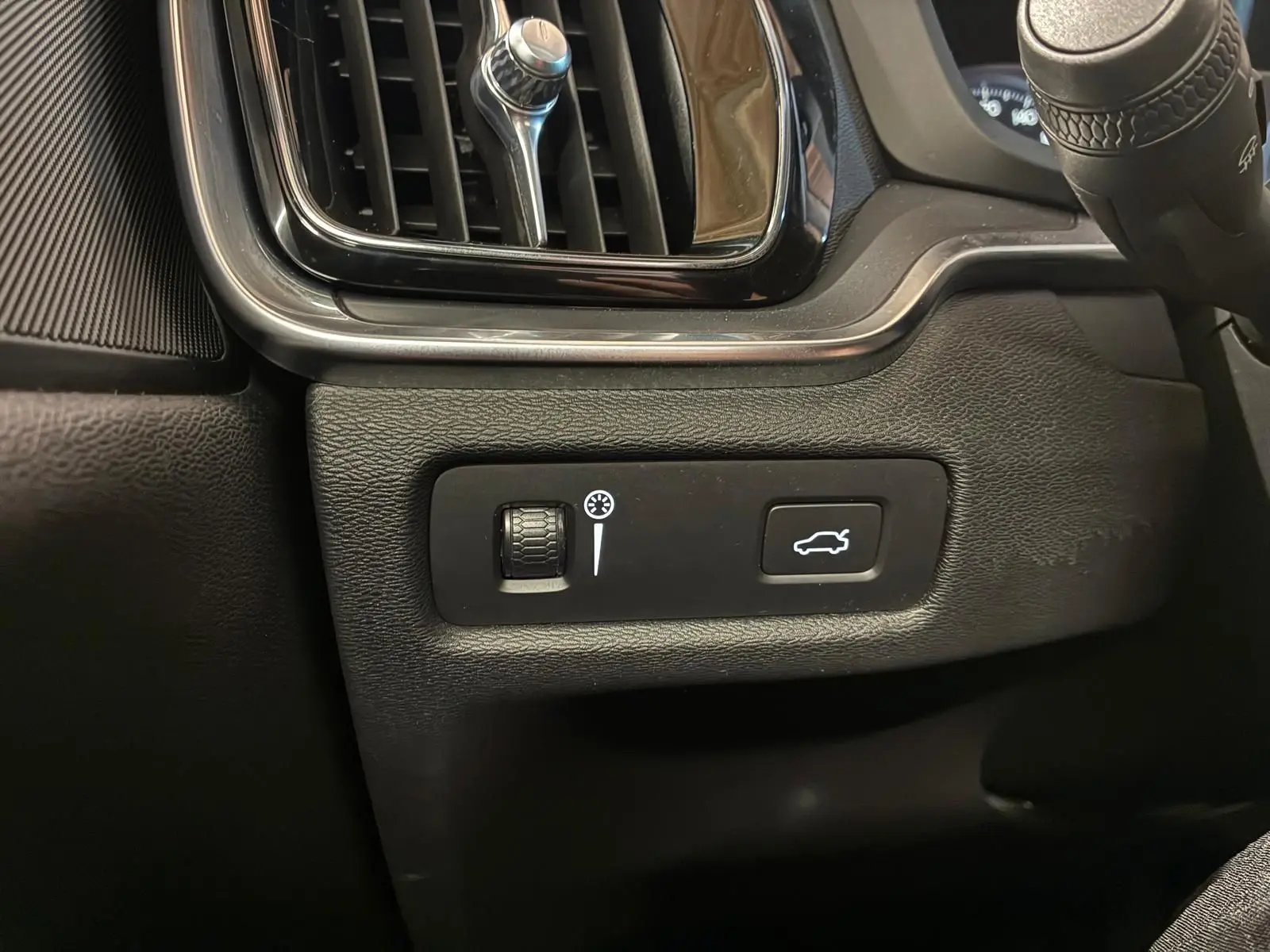 Détail intérieur côté gauche du tableau de bord de la Volvo V60 blanche, avec commande d'éclairage et bouton ouverture coffre.