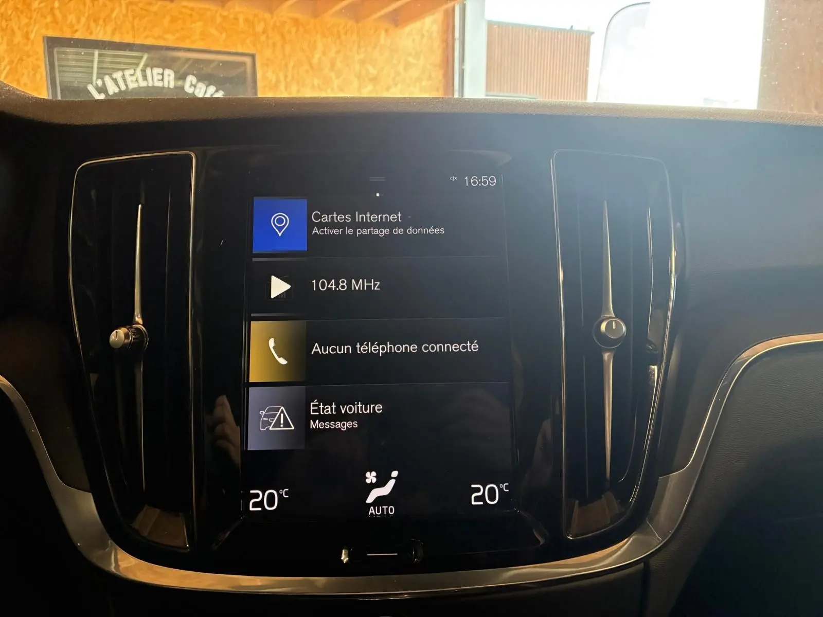 Vue rapprochée de l’écran tactile central noir du tableau de bord du Volvo V60 blanc, affichant la climatisation et la radio.
