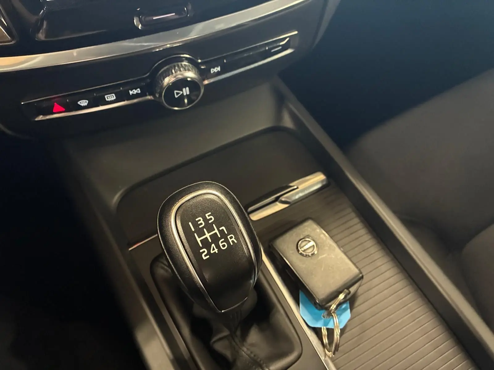 Gros plan sur la console centrale noire d’un Volvo V60 blanc, mettant en valeur le levier de vitesse manuel et une clé Volvo posée à côté.
