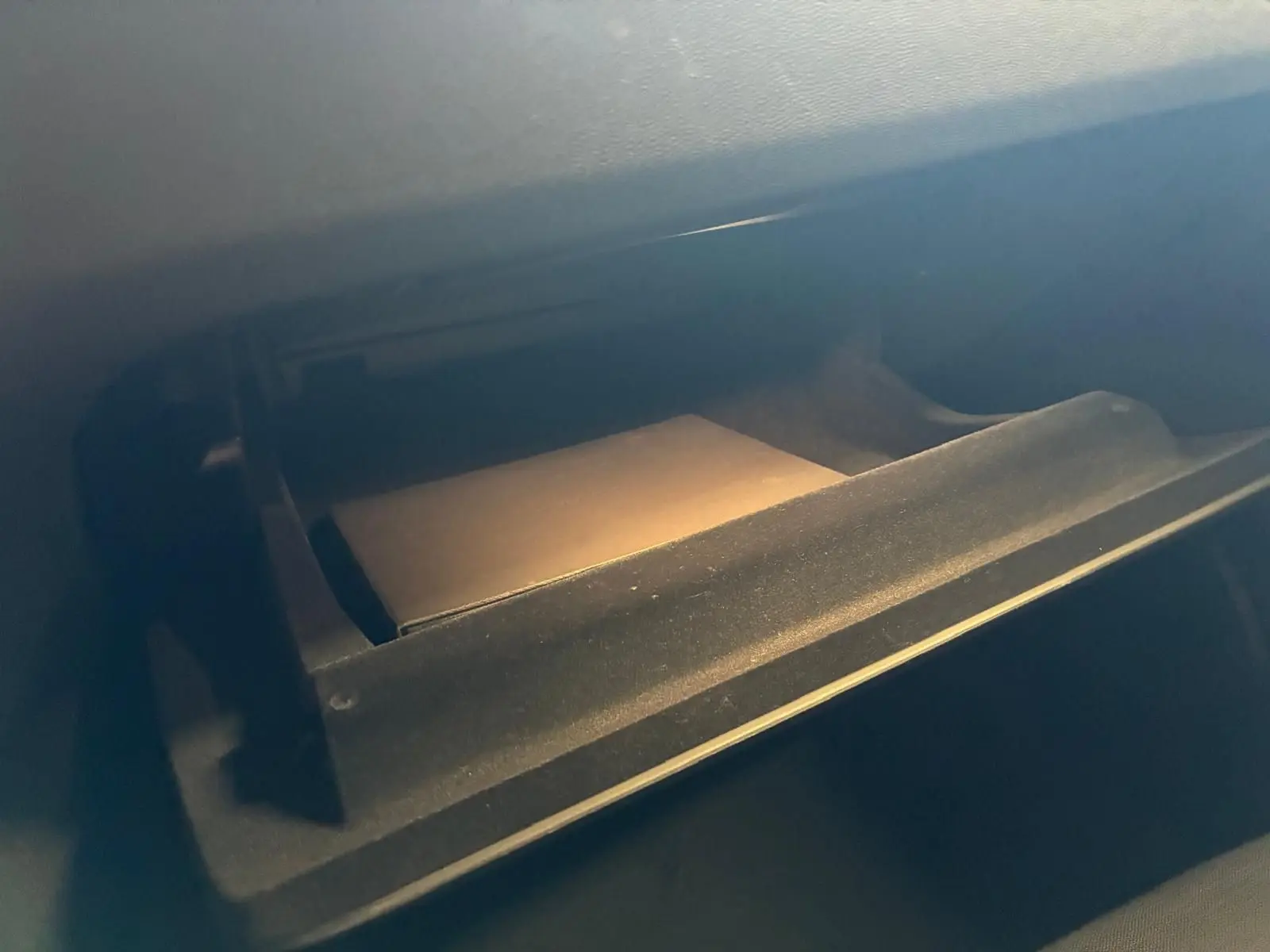 Gros plan sur la boîte à gants ouverte de la Volvo V60 D3 2020, intérieur noir avec un manuel visible.