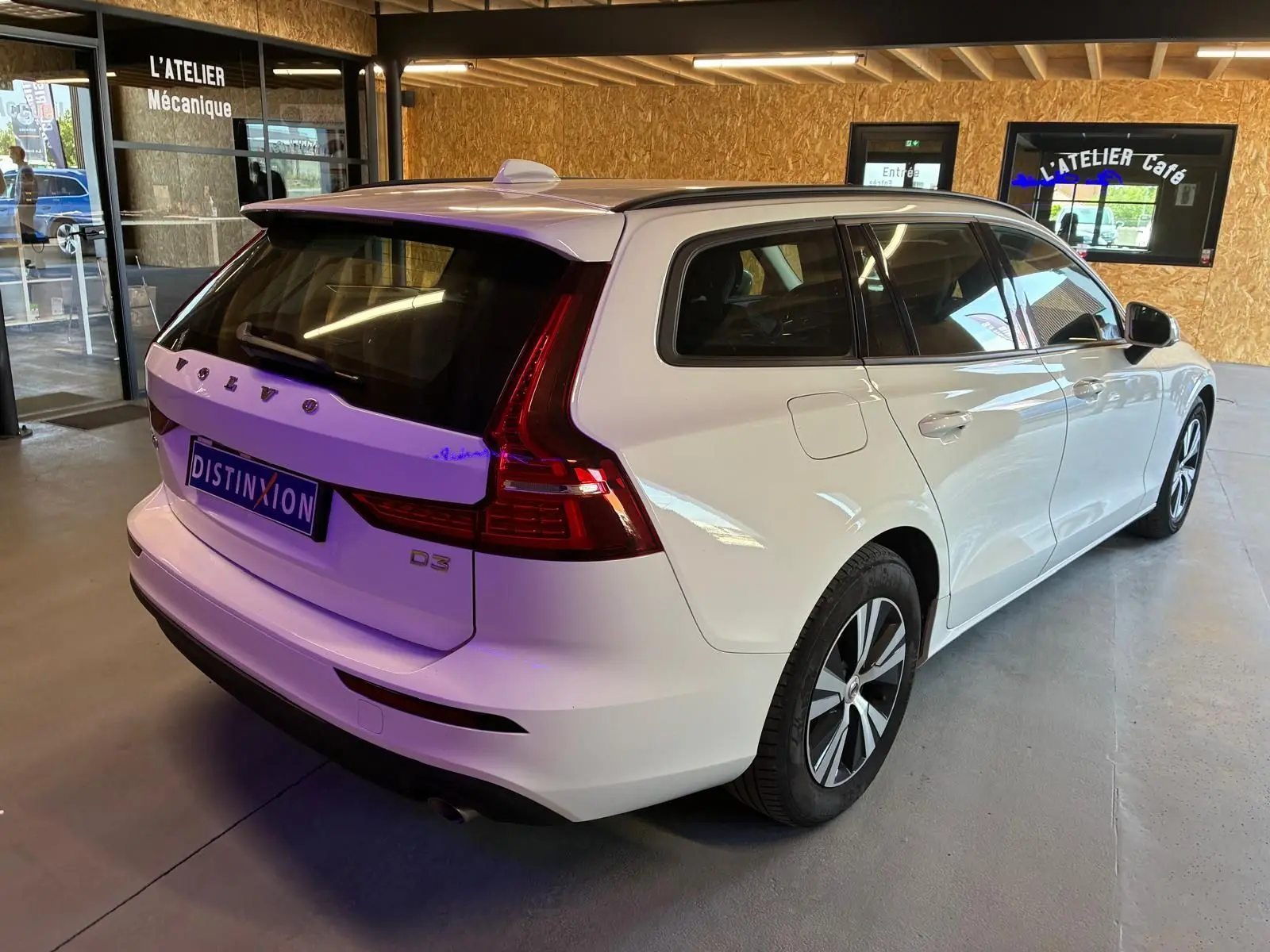 Vue 3/4 arrière droite d’un break Volvo V60 D3 blanc 2020 avec feux arrière LED et toit ouvrant en intérieur d’atelier.