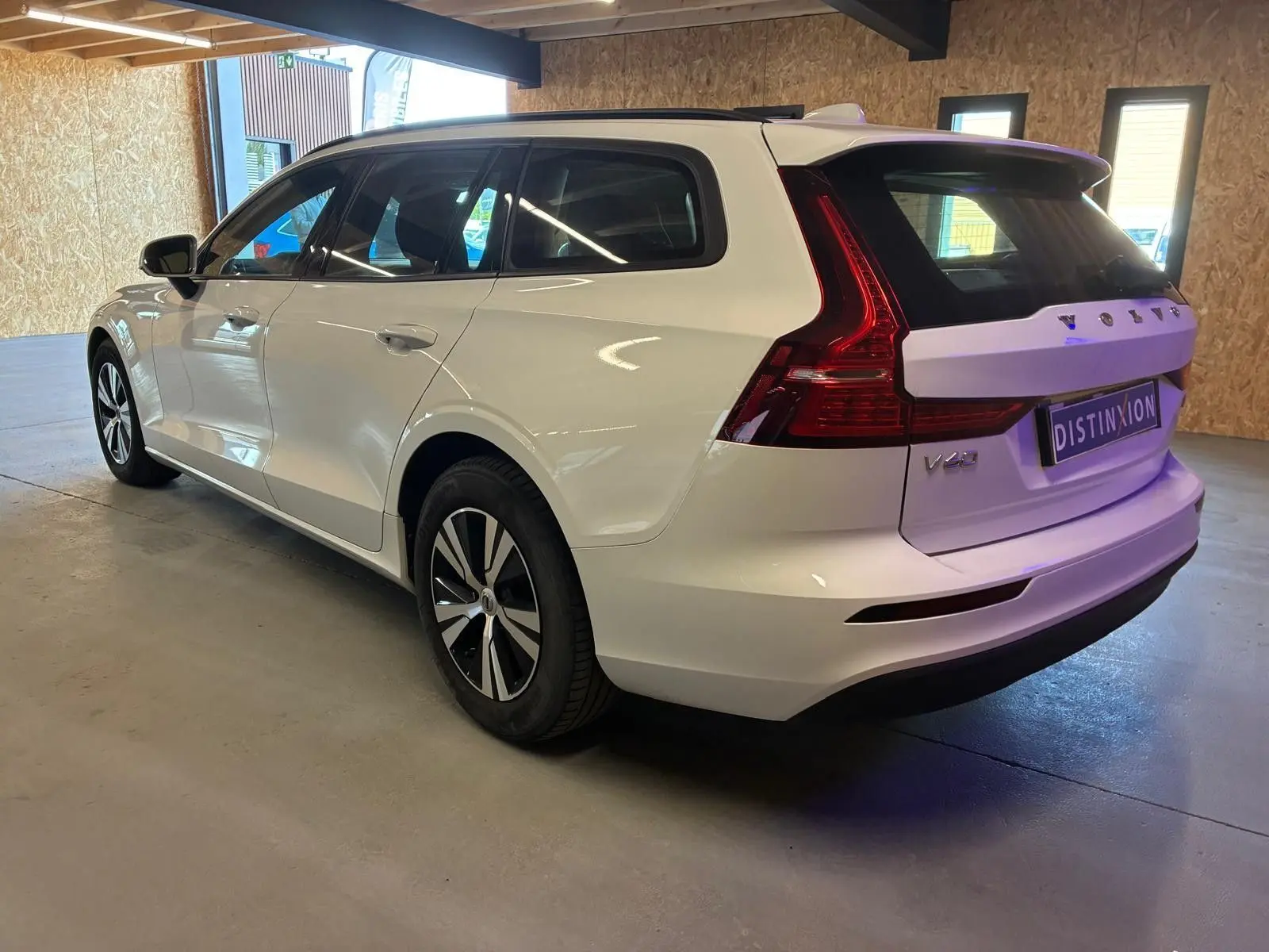 Volvo V60 D3 blanche vue 3/4 arrière droit dans un garage, avec feux arrière caractéristiques et jantes noires.