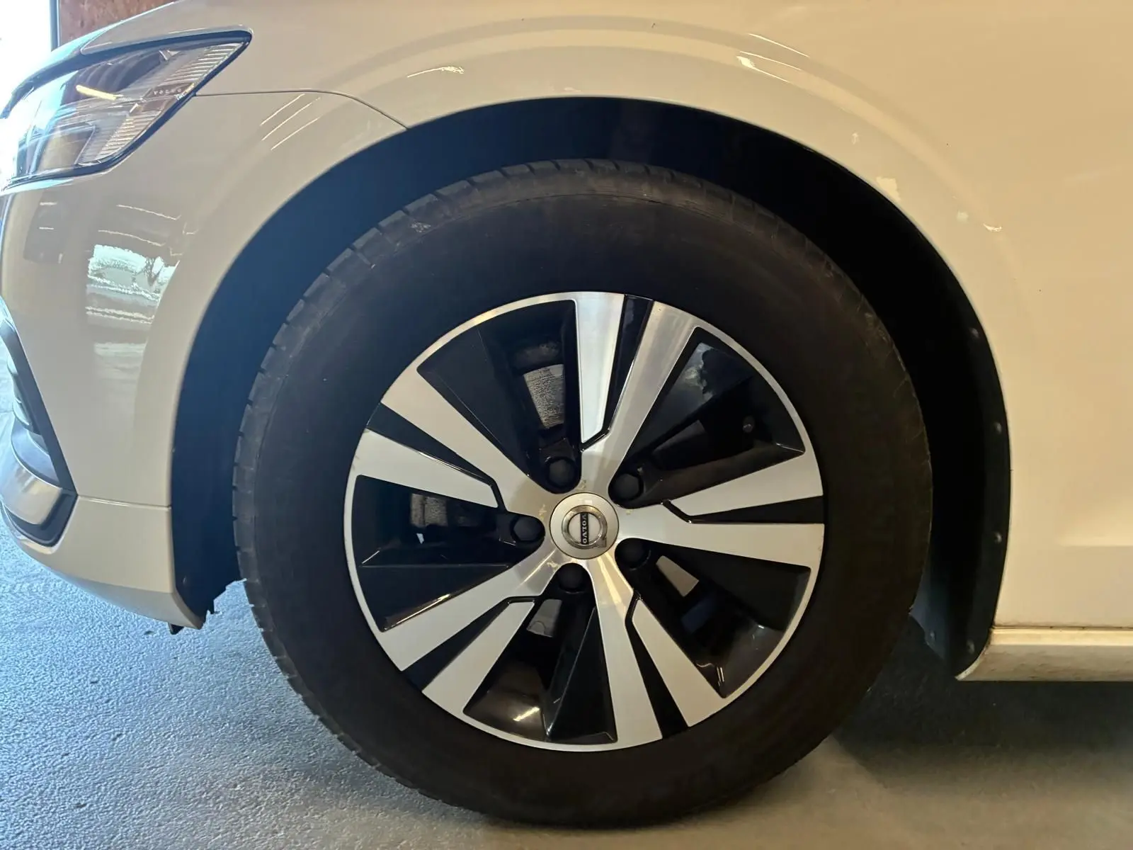 Gros plan sur la roue avant gauche d’un Volvo V60 blanc, mettant en valeur la jante bicolore moderne.