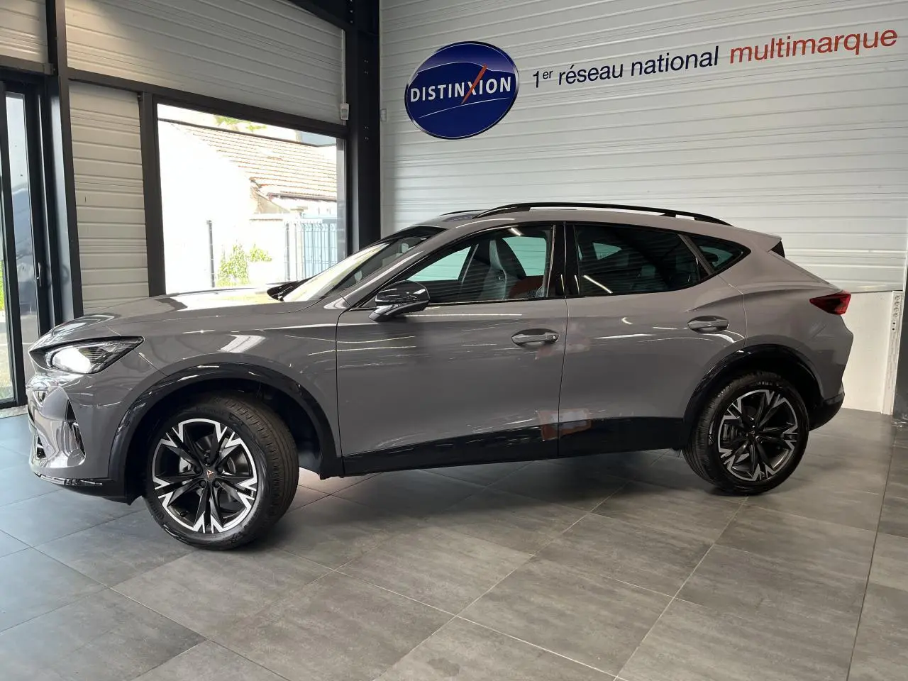 Vue de profil côté gauche du CUPRA Formentor gris clair 2025 avec jantes alliage noires et toit ouvrant panoramique en showroom.