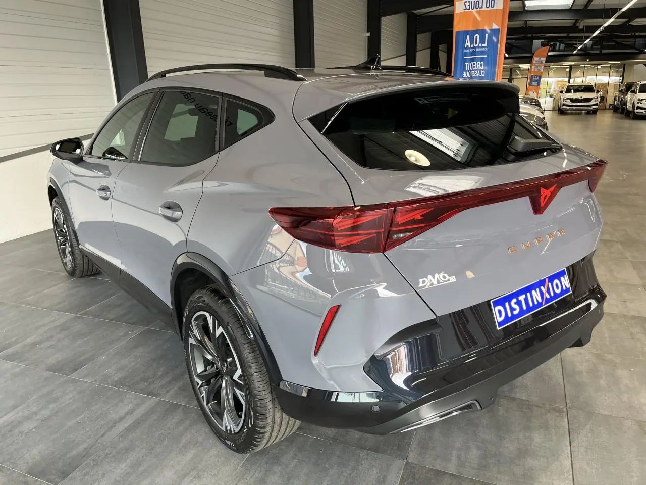 Vue 3/4 arrière droite d’un CUPRA Formentor gris clair avec bandeau lumineux arrière et jantes alliage noires.