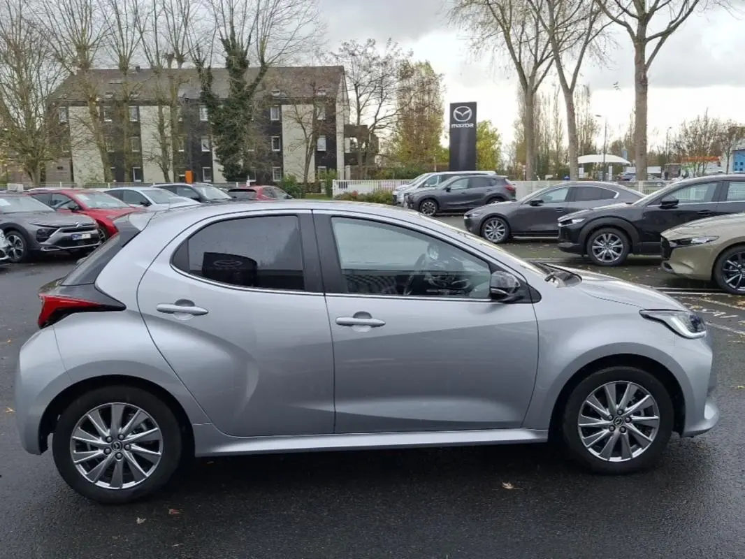 Profil côté gauche d'une Mazda2 hybride argent 2022, avec jantes alliage et lignes sculptées visibles.