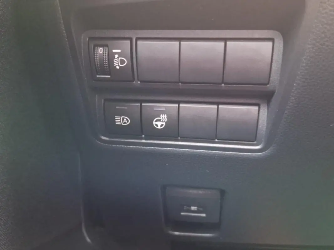 Gros plan sur les commandes de réglage des phares et du volant chauffant dans une Mazda2 hybride argentée de 2022.