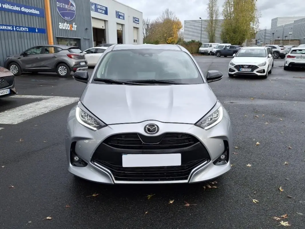 Vue frontale d'une Mazda2 Hybrid 2022 argent avec calandre noire et phares LED distinctifs sur un parking.