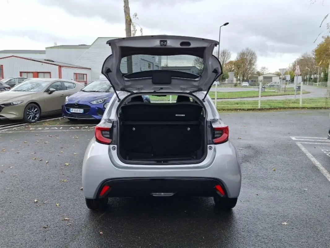 Vue arrière d'une Mazda2 hybride 2022 argent avec le coffre ouvert sur un parking extérieur.