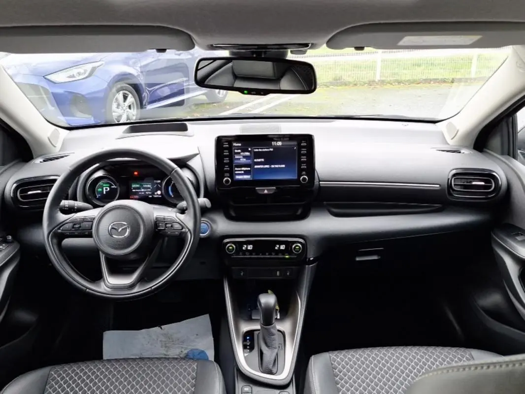 Vue intérieure avant de la Mazda2 hybride 2022, tableau de bord noir avec écran tactile et volant multifonction.