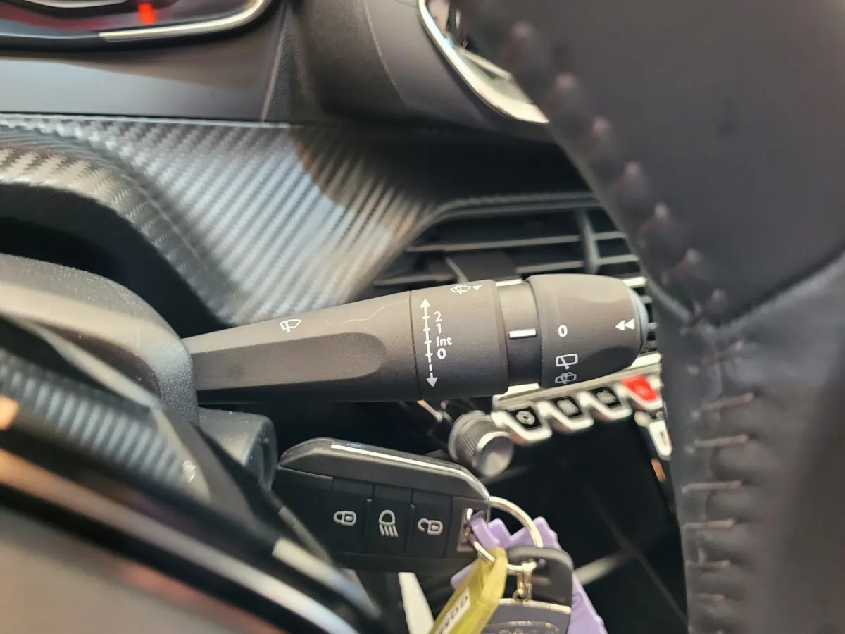 Gros plan sur la commande d’essuie-glace et clé de contact dans l’habitacle noir de la Peugeot 208 gris foncé 2023.